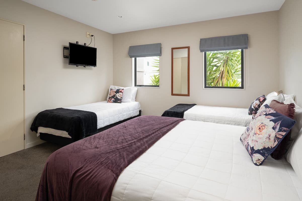 A bedroom with two single beds, a larger bed, a flat-screen TV, and windows with curtains.