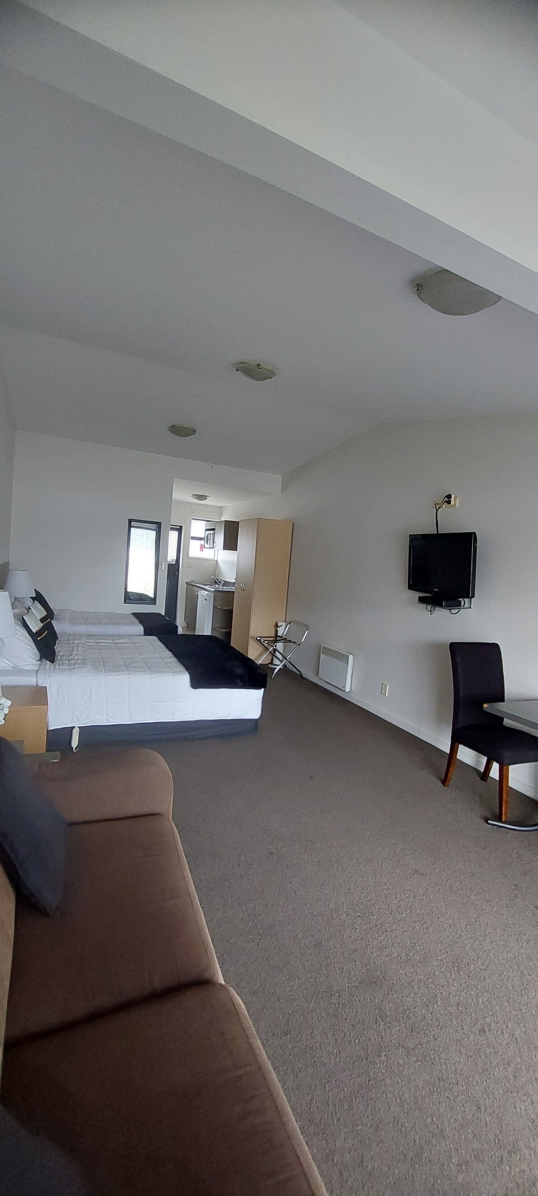 A hotel room with a bed, a TV, a chair, and a sofa.