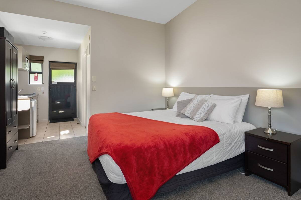 A bedroom with a bed, bedside tables, a nightstand, a desk, and a door leading to a bathroom.