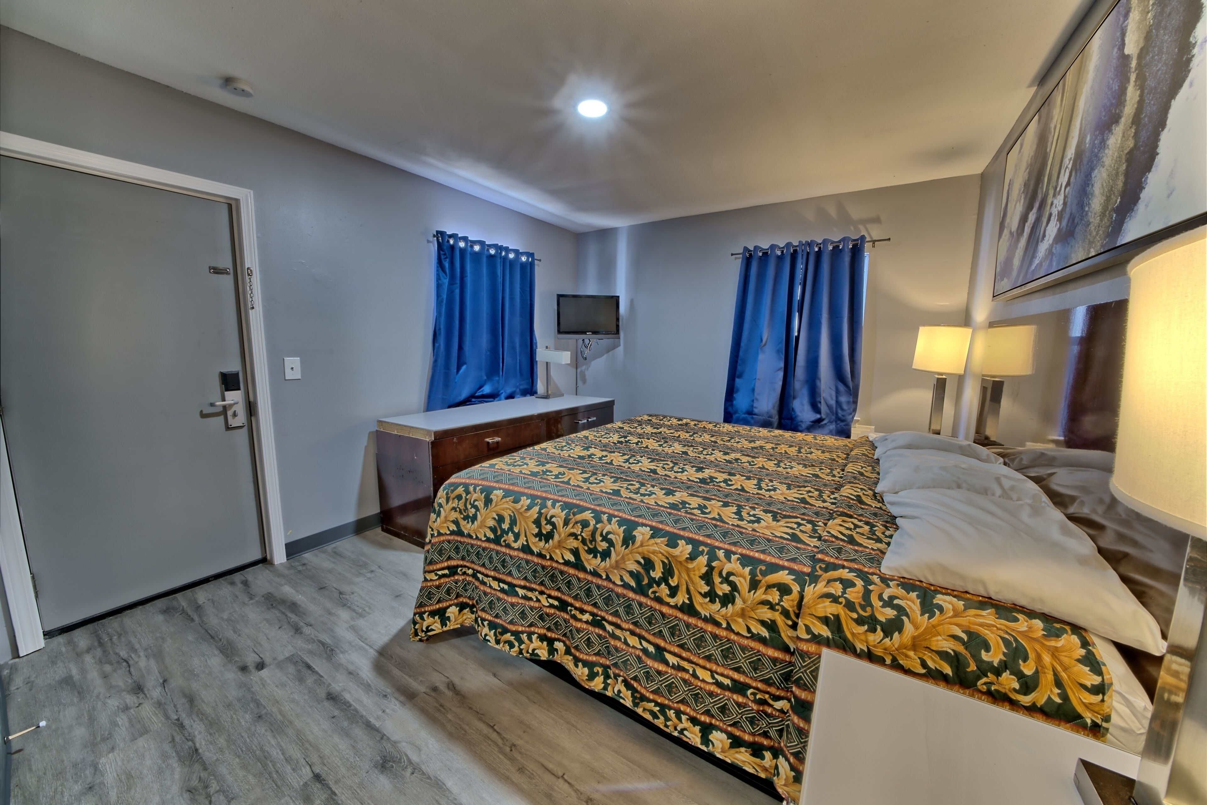 A bedroom with a bed, a desk, a chair, a TV, and a door.