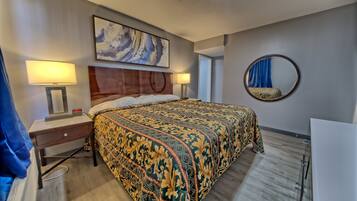 A hotel room with a large bed, two bedside tables with lamps, a round mirror, and a painting on the wall.