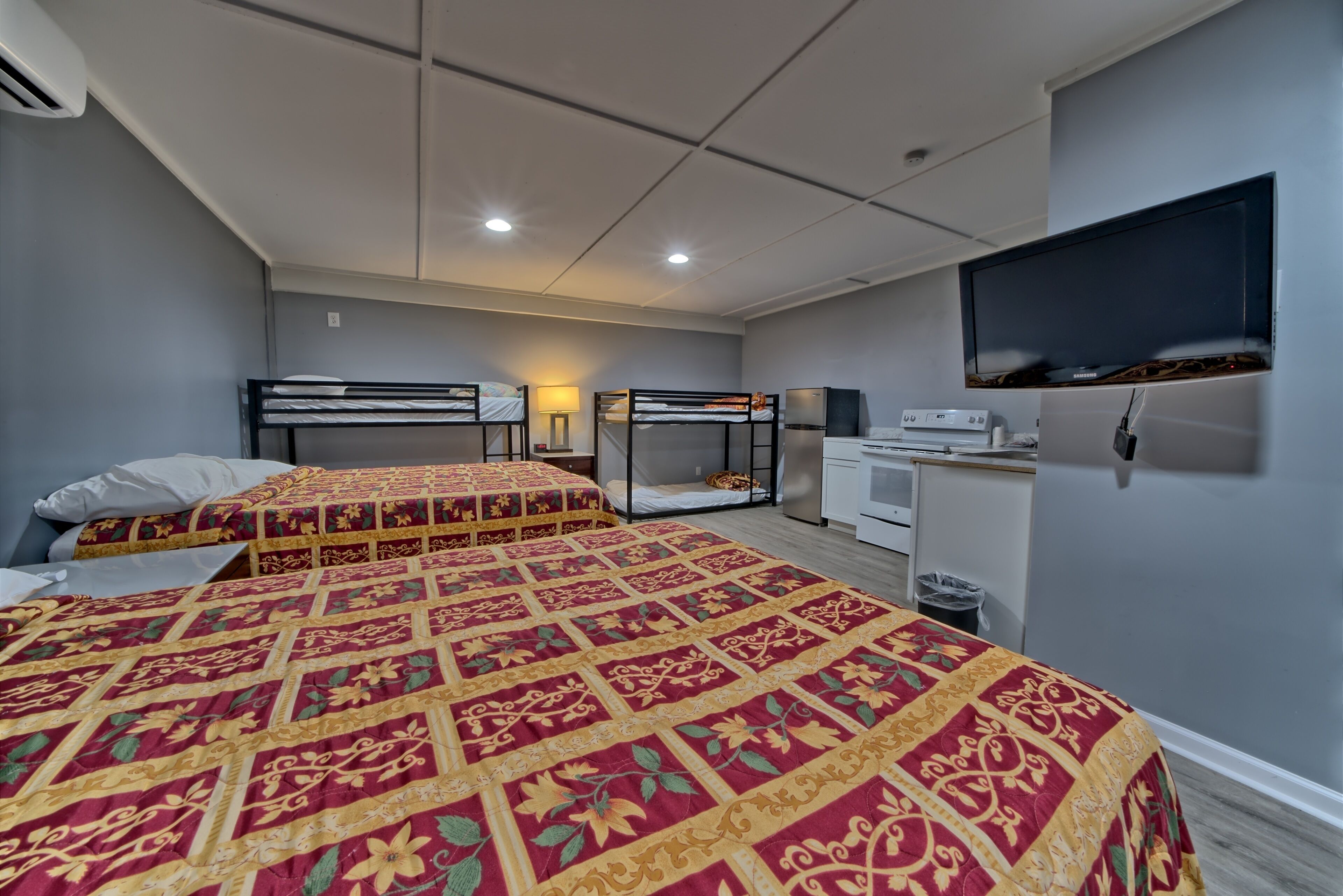 A hotel room with two beds, a TV, a desk, and a small kitchenette.