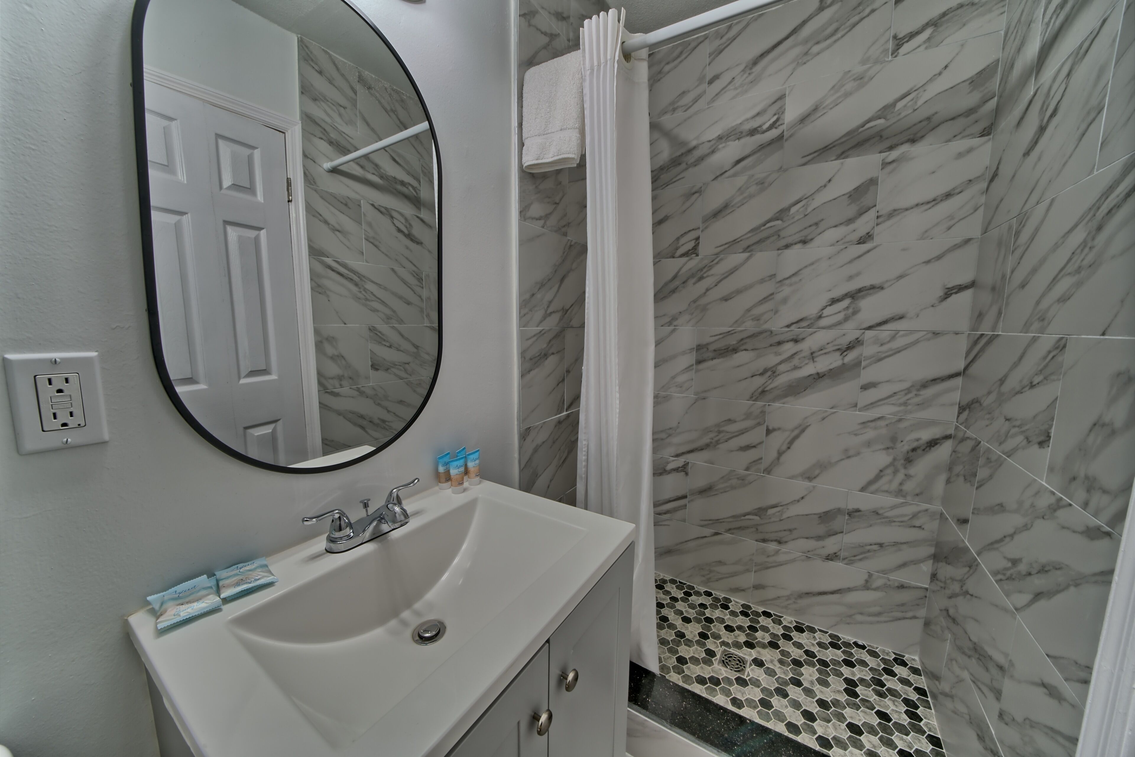 Un baño con lavamanos blanco, espejo y paredes con diseño de mármol.