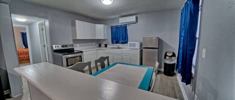A compact kitchen with white cabinets, a microwave, a stove, and a trash can.