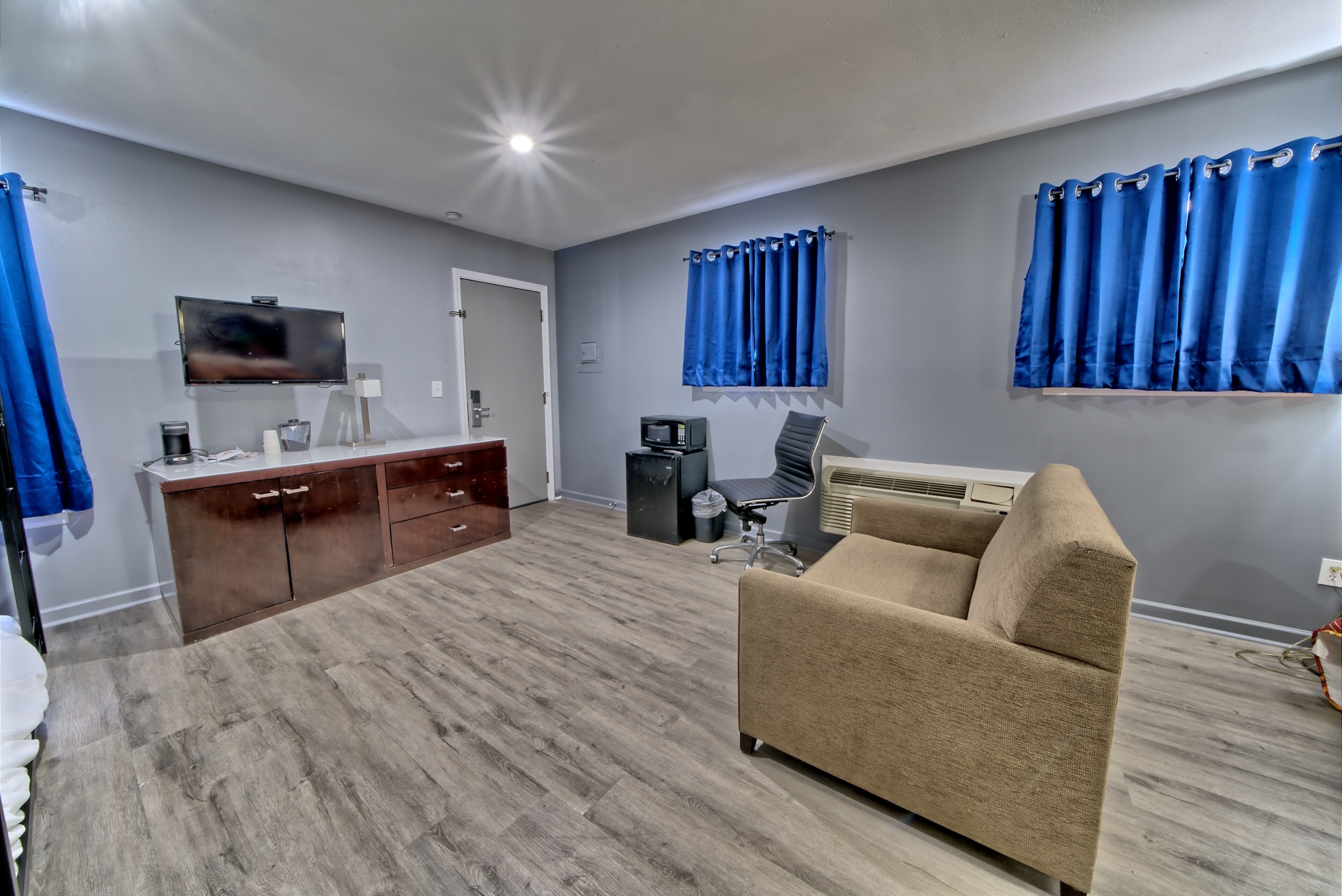 A modern living room with a beige sofa, a flat-screen TV, a wooden cabinet, and blue curtains.