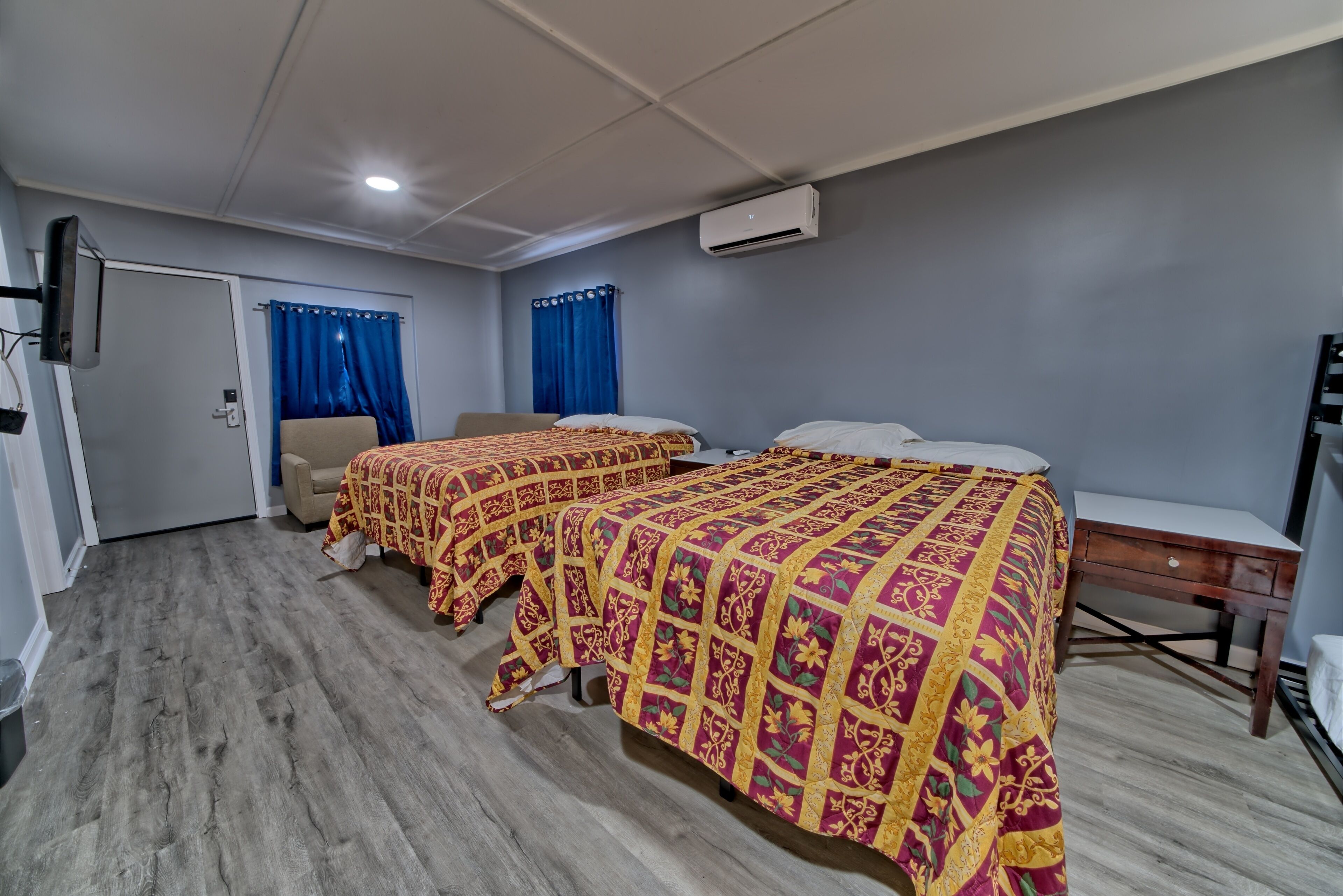 Quarto de hotel com três camas, uma escrivaninha, uma cadeira e uma televisão.