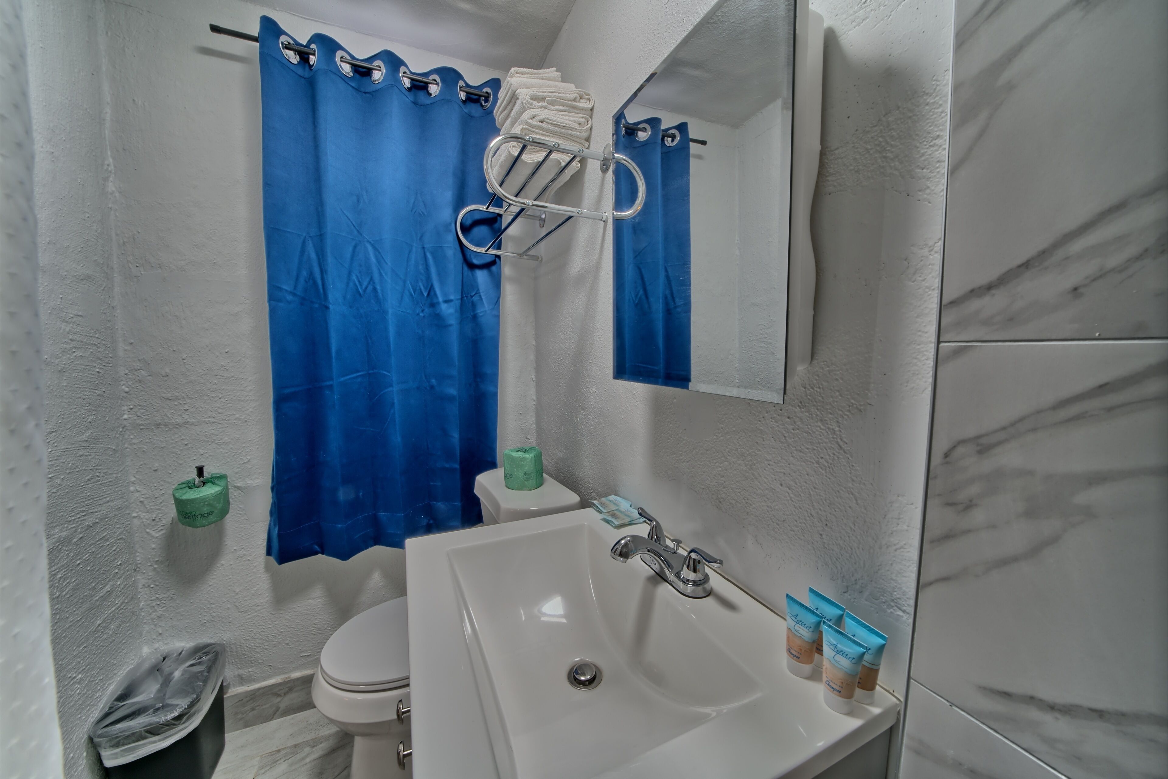 Un baño con lavamanos blanco, inodoro, cortina de ducha azul y toallero.