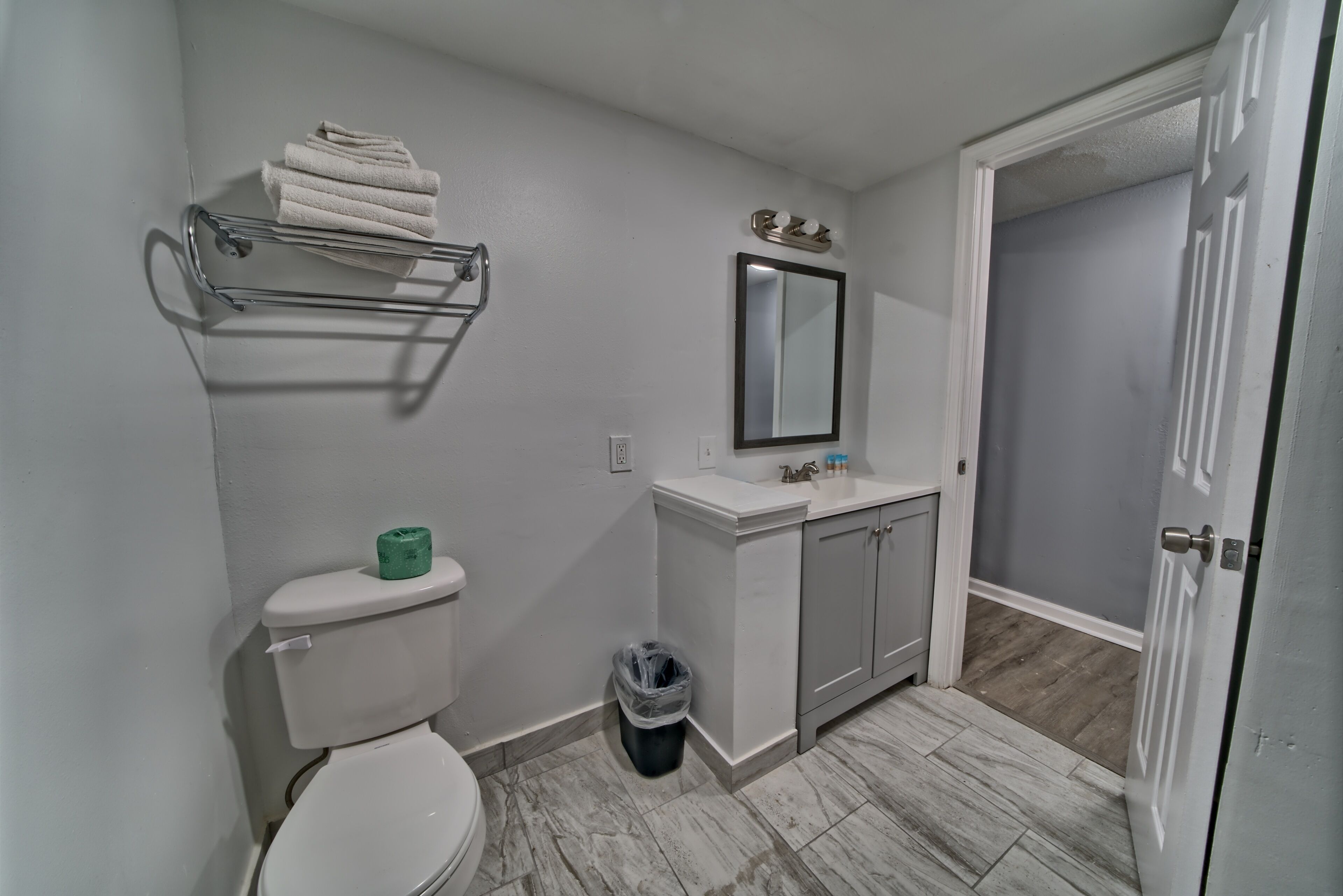 A bathroom with a toilet, a sink with a mirror, a towel rack, and a trash can.