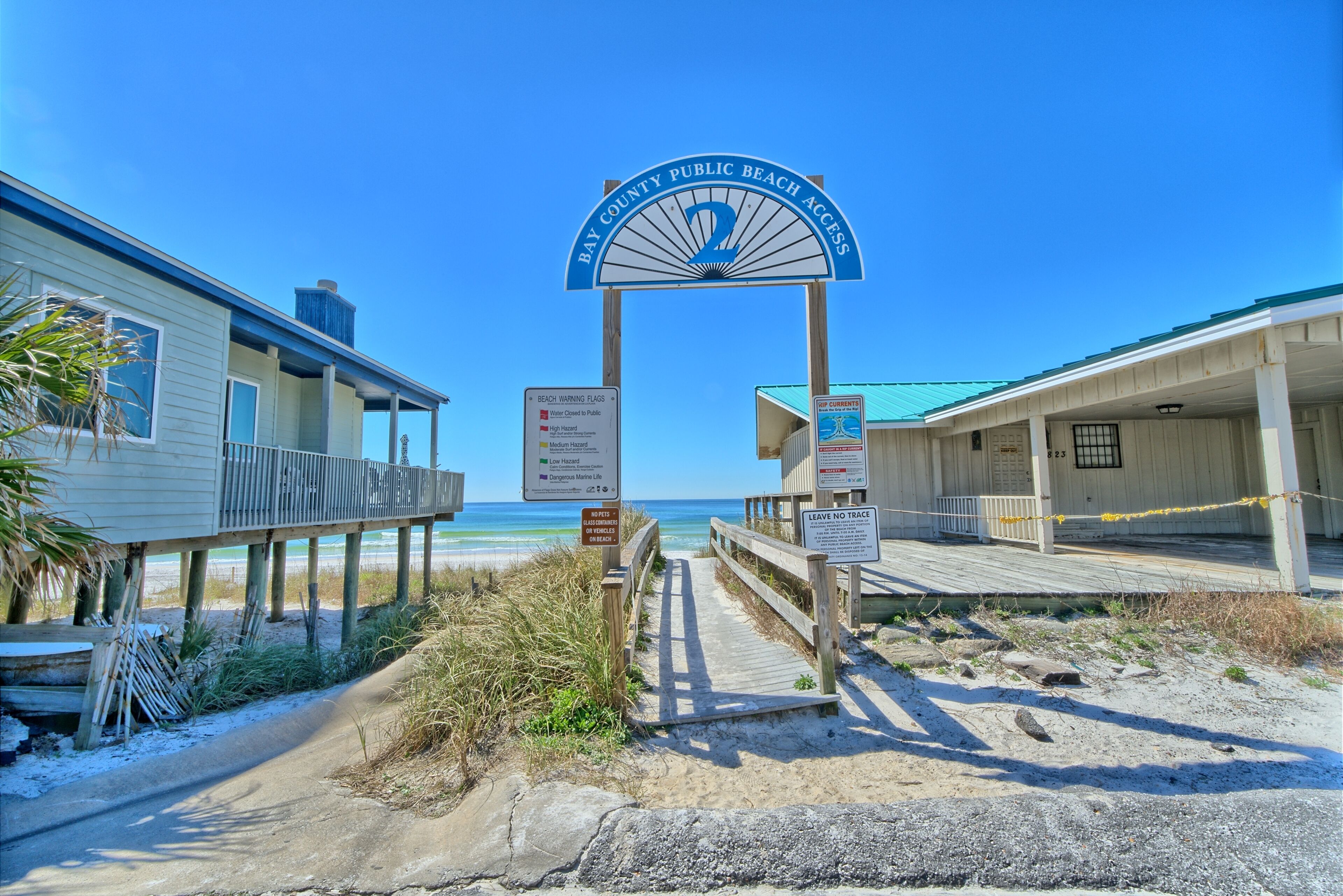 Schild für den Zugang zum Strand, Holzstege und Strandhäuser mit freiem Blick auf das Meer.