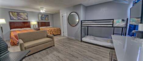 A hotel room with a bed, a sofa, a desk, a mirror, and artwork on the walls.