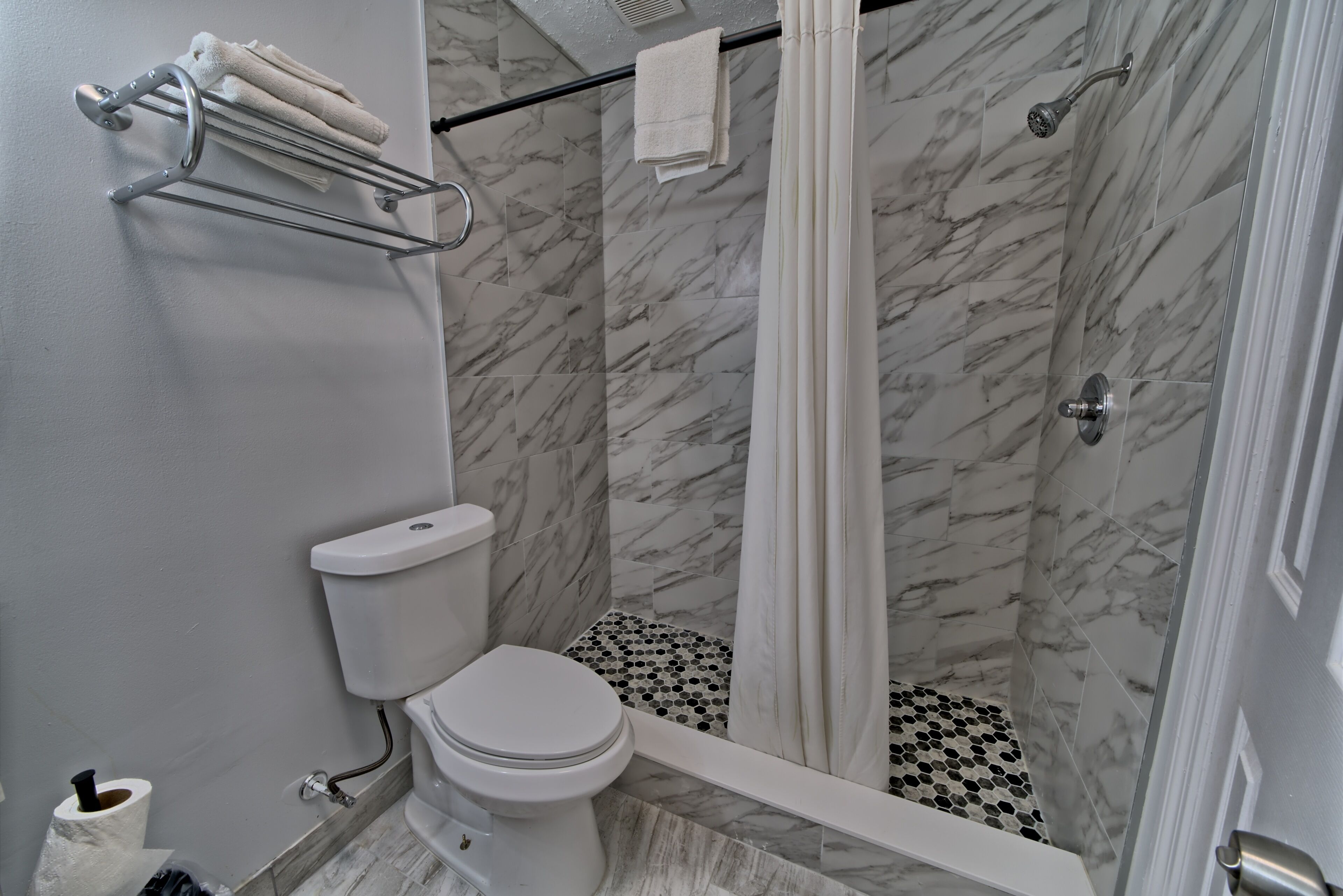 A bathroom with a toilet, shower, and a towel rack.