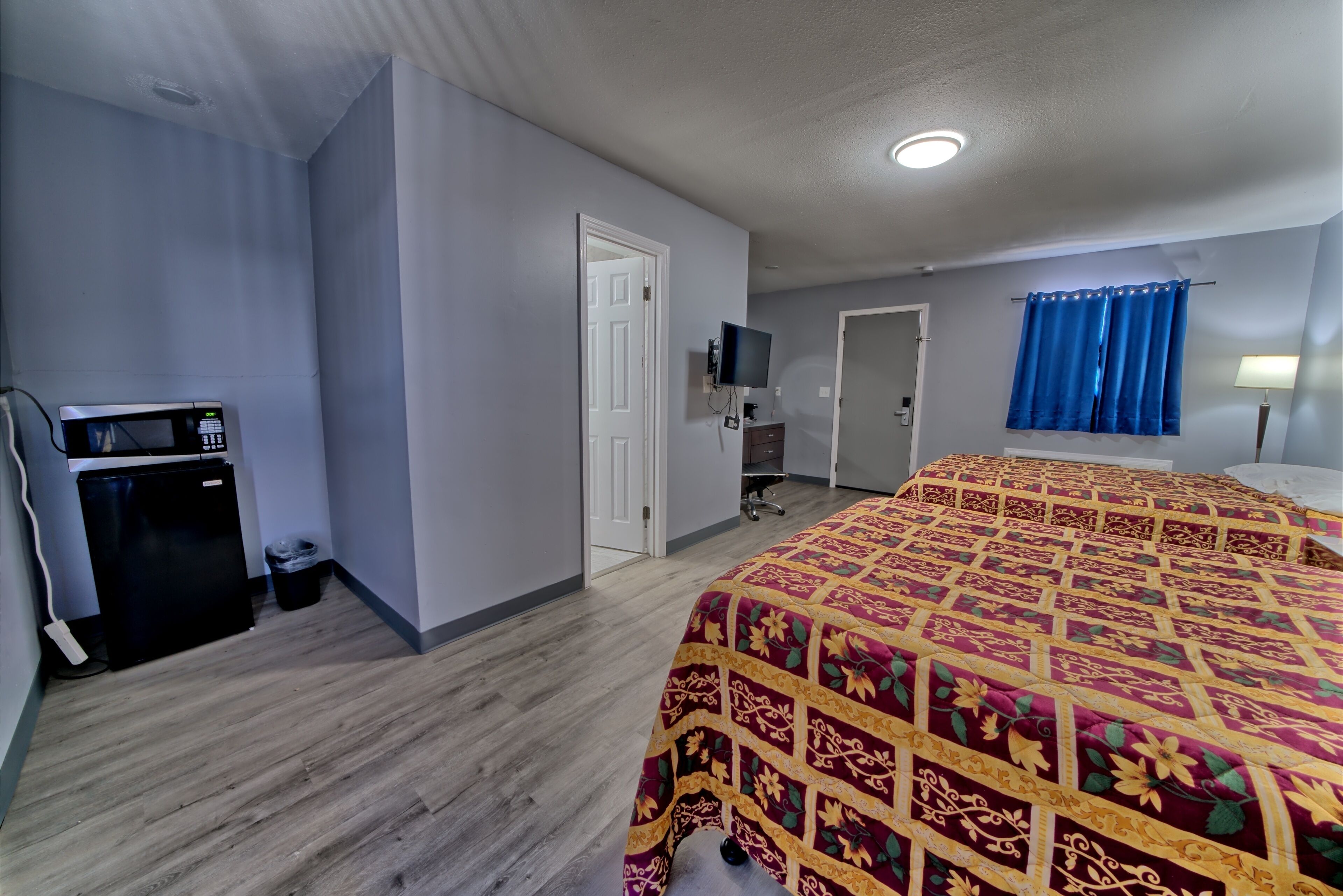 Quarto de hotel com cama, escrivaninha com computador, micro-ondas e lixeira.