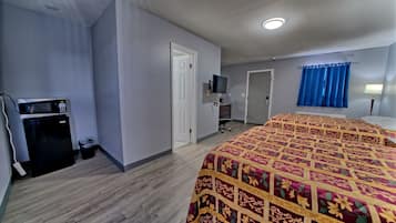 Quarto de hotel com cama, escrivaninha com computador, micro-ondas e lixeira.