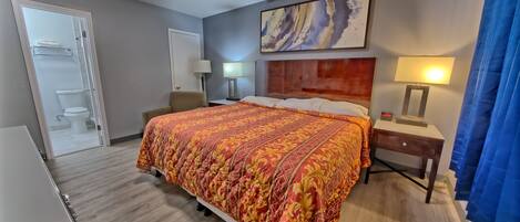 Habitación de hotel con una cama grande, un escritorio, una silla, baño con inodoro y lavamanos, y un cuadro en la pared.