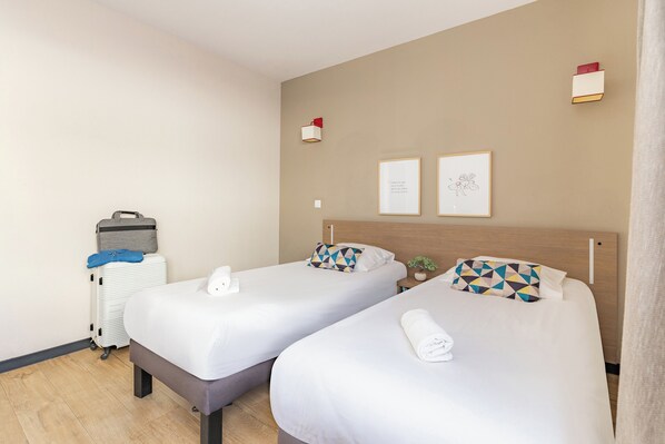 A hotel room with two beds, a suitcase, a radiator, and two framed pictures on the wall. - Appart'City Classic Annemasse Centre-Pays de Genève (Annemasse)