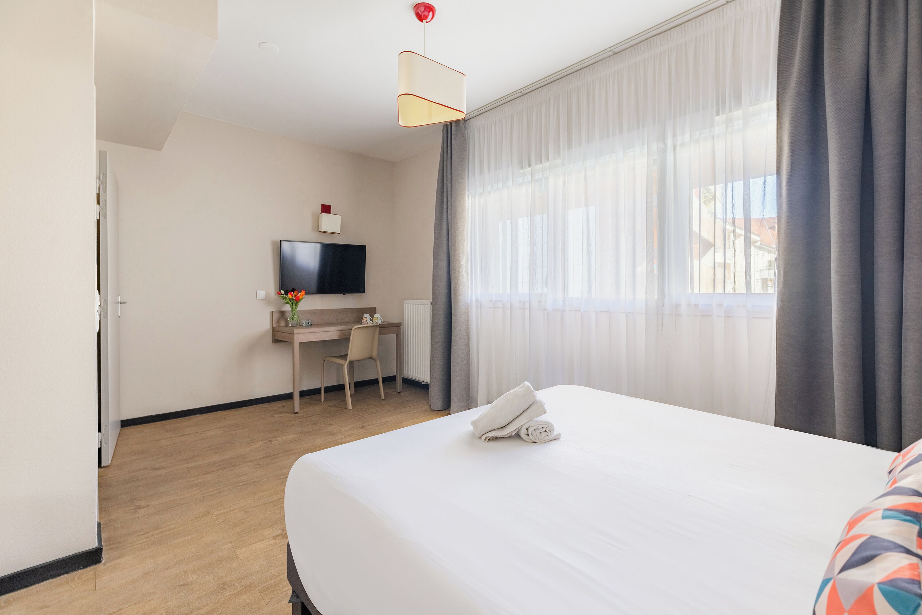 Une chambre d’hôtel équipée d’un lit, d’un bureau, d’une chaise, d’une télévision et d’une fenêtre avec des rideaux.