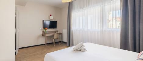 A hotel room with a bed, a desk, a chair, a television, and a window with curtains.