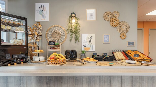 A breakfast buffet with various food items, a coffee machine, and decorative wall art. - Appart'City Classic Annemasse Centre-Pays de Genève (Annemasse)
