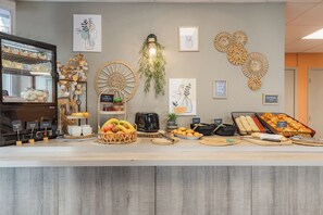 A breakfast buffet with various food items, a coffee machine, and decorative wall art. - Appart'City Classic Annemasse Centre-Pays de Genève (Annemasse)