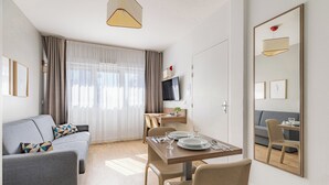 A modern living room with a sofa, dining table, chairs, a TV, and a large mirror. - Appart'City Classic Annemasse Centre-Pays de Genève (Annemasse)