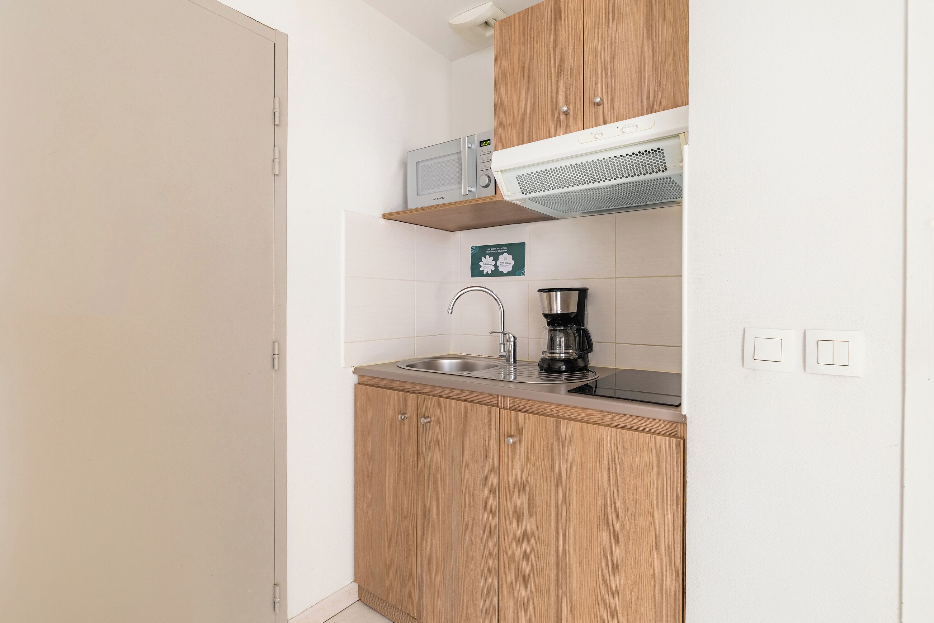Una kitchenette equipada con microondas, cafetera y pileta de acero inoxidable.