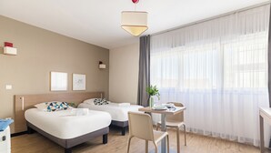 A hotel room with two beds, a dining table, chairs, a plant, and a large window with sheer curtains. - Appart'City Classic Annemasse Centre-Pays de Genève (Annemasse)