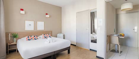 Una habitación de hotel moderna con una cama grande, mesitas de noche, un escritorio y un baño visible a través de una puerta abierta.