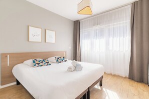 Habitació d'hotel amb un llit, un capçal, una finestra amb cortines i dos quadres a la paret.
