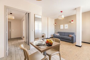 Un saló modern amb un sofà gris, una taula de dinar amb cadires i una zona de cuina al fons.