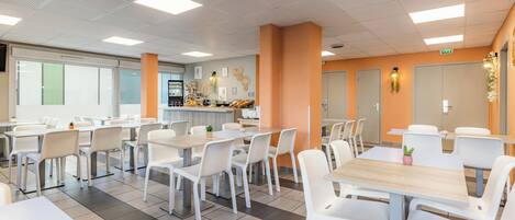 A modern cafeteria with white tables and chairs, a coffee machine, and a fruit display.