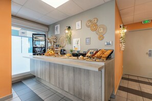 A reception area with a counter displaying various food items, a refrigerator, and wall decorations. - Appart'City Classic Annemasse Centre-Pays de Genève (Annemasse)