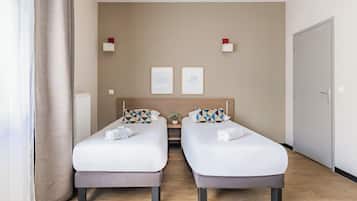 A hotel room with two beds, a small table, a potted plant, and a door.