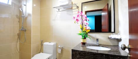 A bathroom with a toilet, sink, shower, and a mirror.
