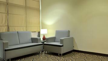 A hotel room with a grey sofa, a smaller armchair, a lamp, and a patterned carpet.