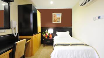 A hotel room with a bed, a desk, a chair, a nightstand with a lamp, and a painting on the wall.