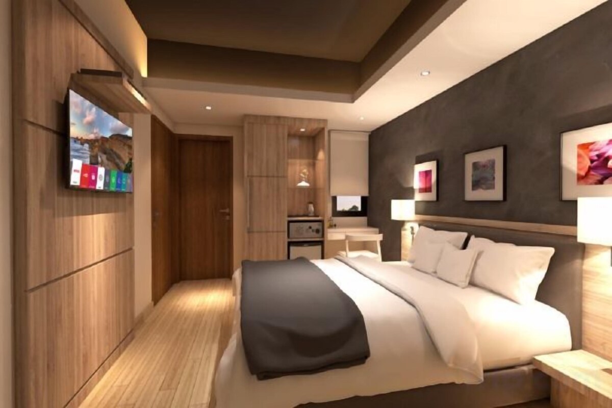 A modern hotel room with a large bed, a TV mounted on the wall, a desk, and a wardrobe.