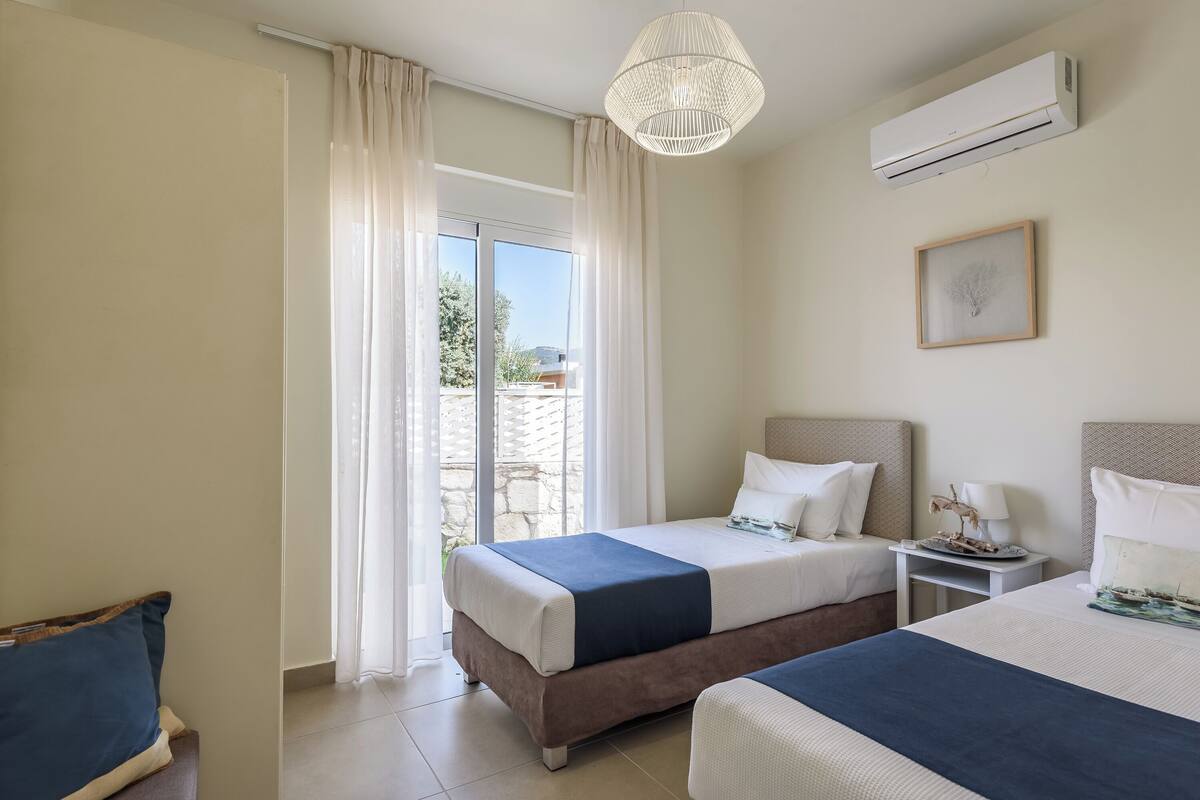 A hotel room with two beds, a ceiling fan, an air conditioning unit, a framed picture, and a view of the outdoors.