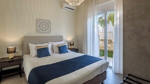 Ein Hotelzimmer mit einem großen Bett, einem Deckenventilator, einer Klimaanlage, einem Nachttisch mit Lampe und Blick ins Freie durch eine Schiebetür.