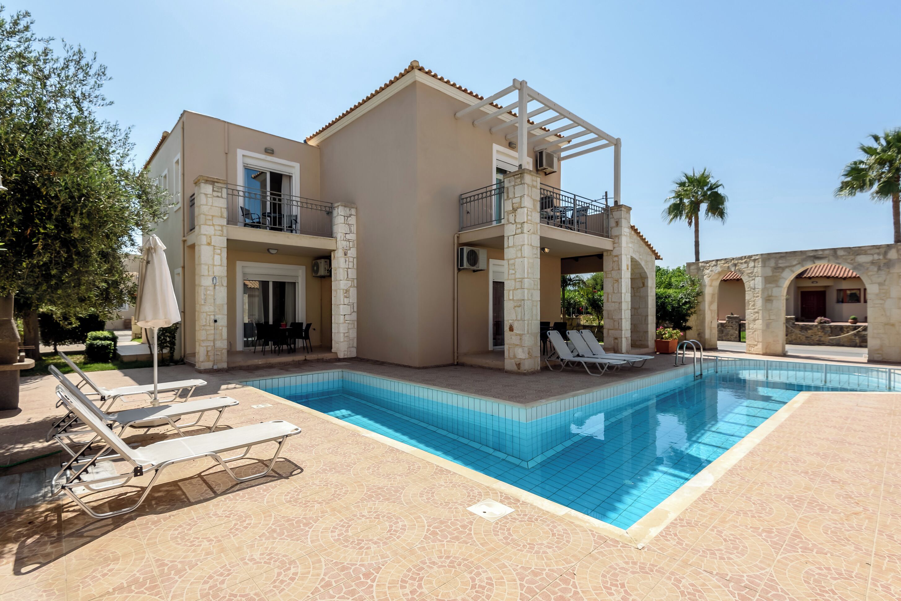 A two-story building with a swimming pool, outdoor seating, and a pergola.