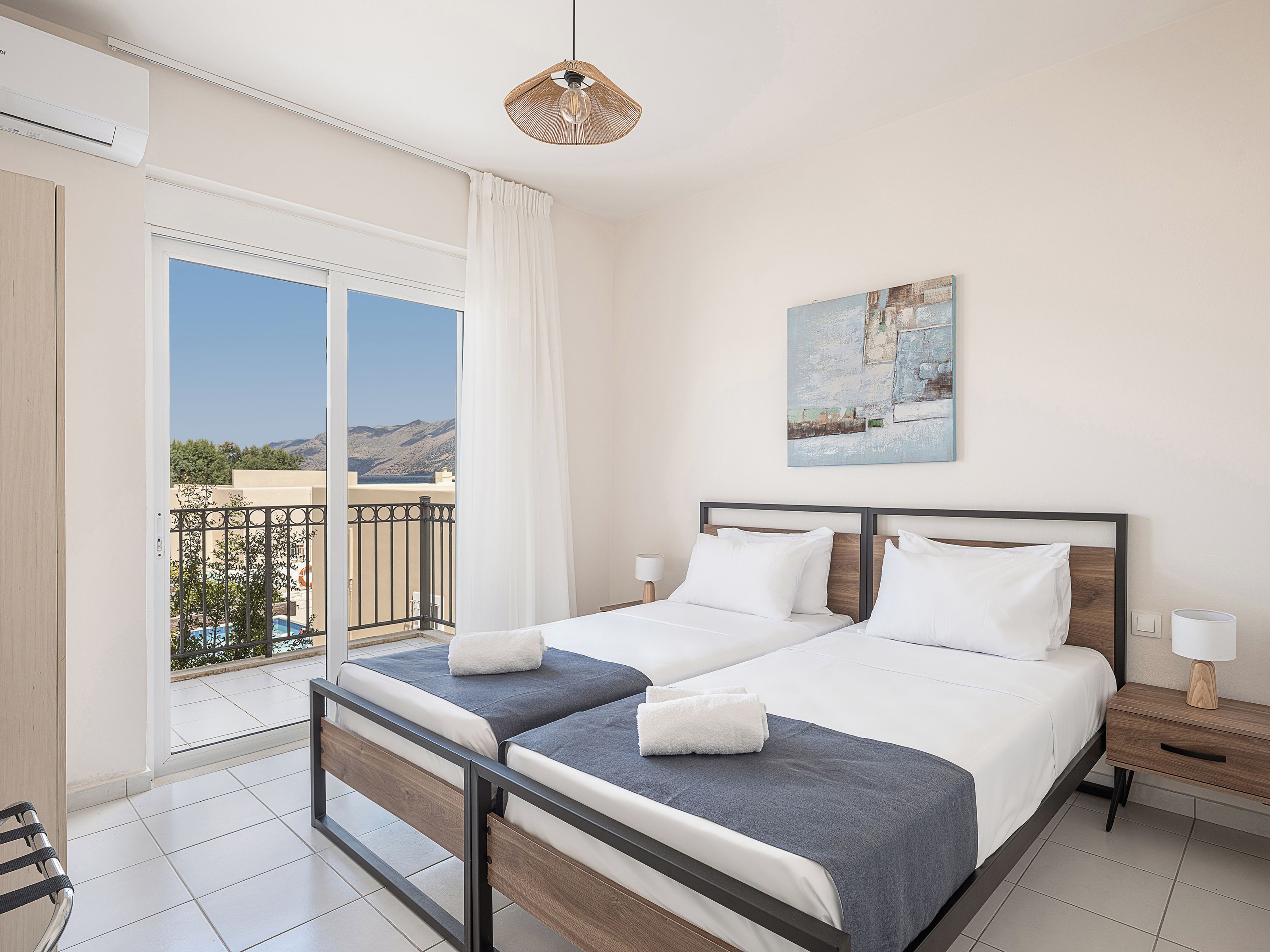 Habitación de hotel con cama, mesita de noche, lámpara, un cuadro en la pared y vistas al exterior.