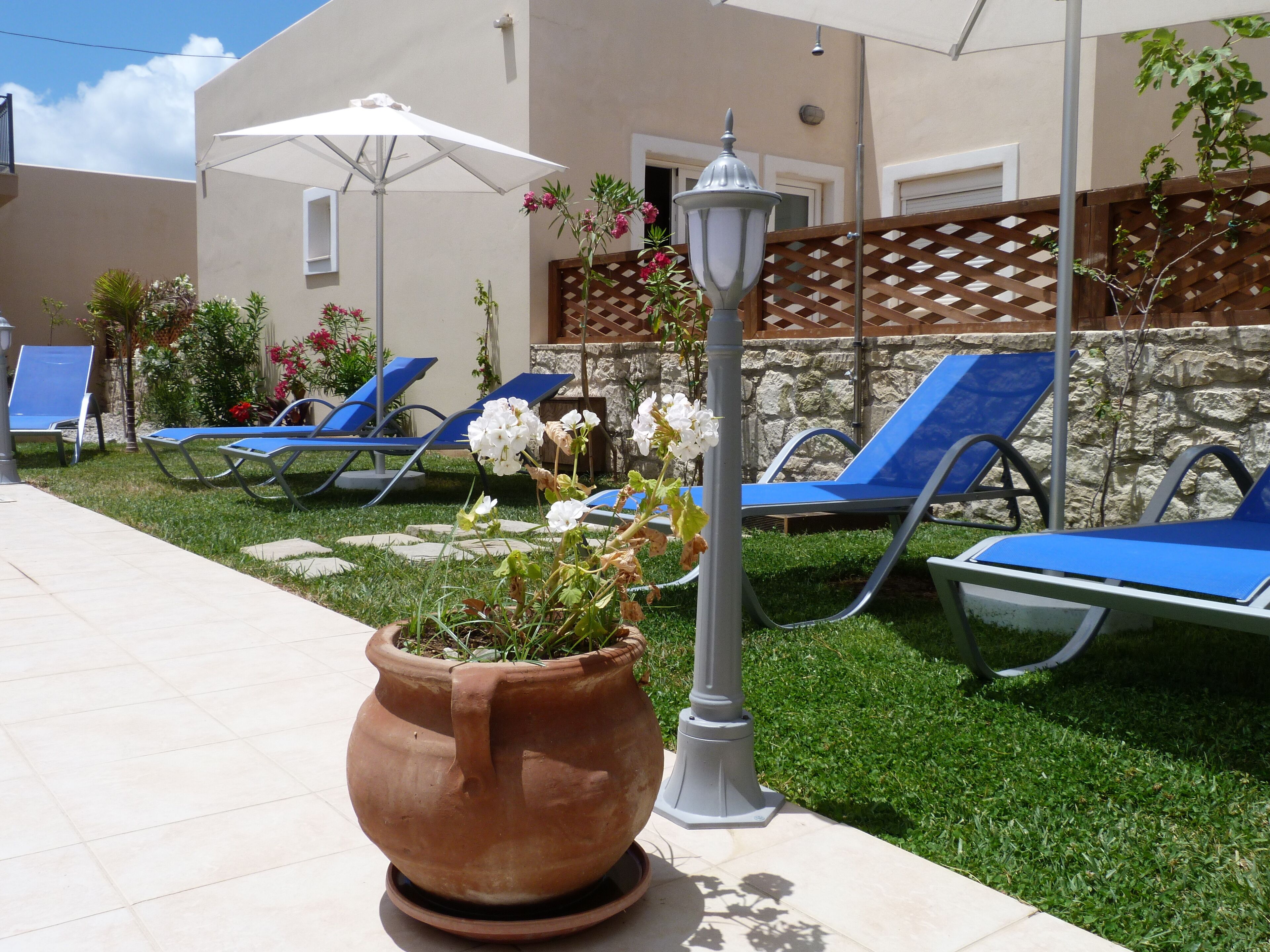 A patio area with blue lounge chairs, a large terracotta pot with flowers, and a white lamp post.