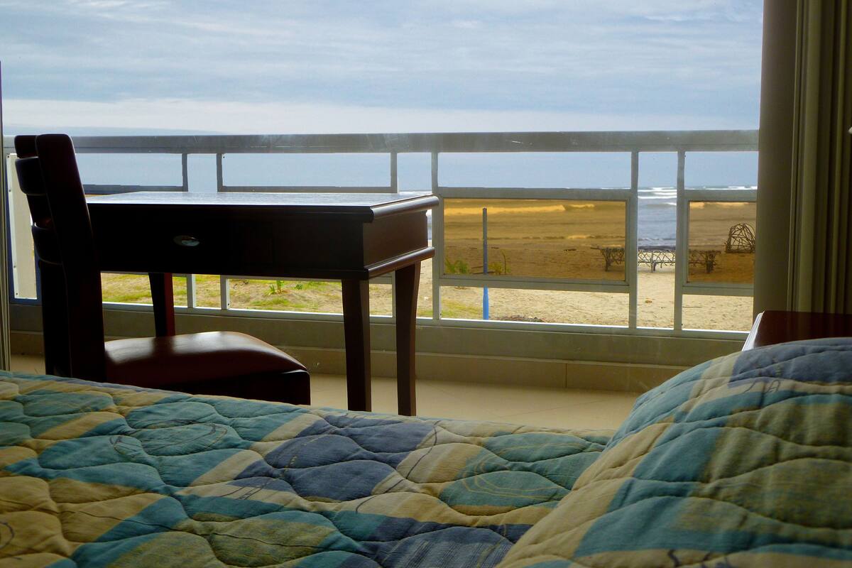 A bedroom with a view of the beach through a balcony railing.