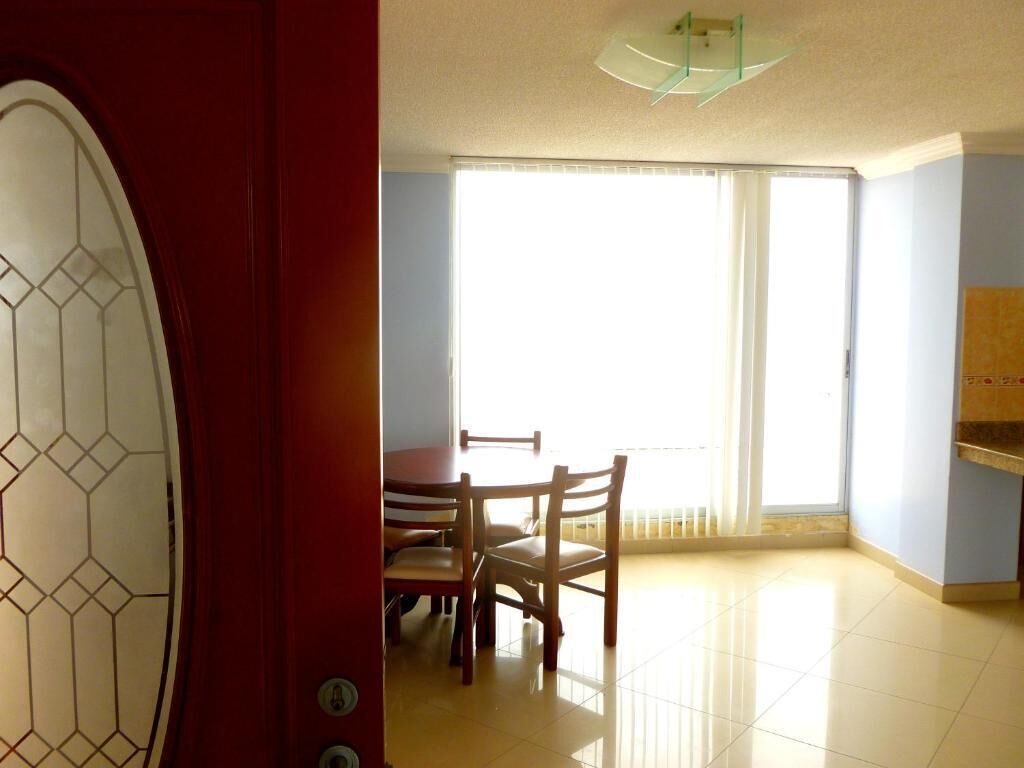 Una habitación con una mesa de comedor y sillas, un ventanal con persianas y una puerta roja con un diseño geométrico de cristal.