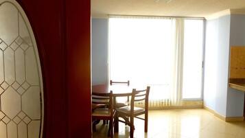 Una habitación con una mesa de comedor y sillas, un ventanal con persianas y una puerta roja con un diseño geométrico de cristal.