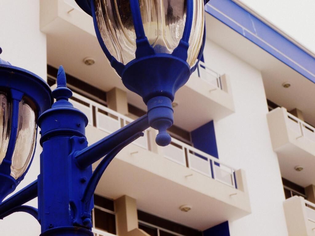 Primer plano de una lámpara de calle azul con pantalla de cristal reflectante, sujeta a un poste metálico.