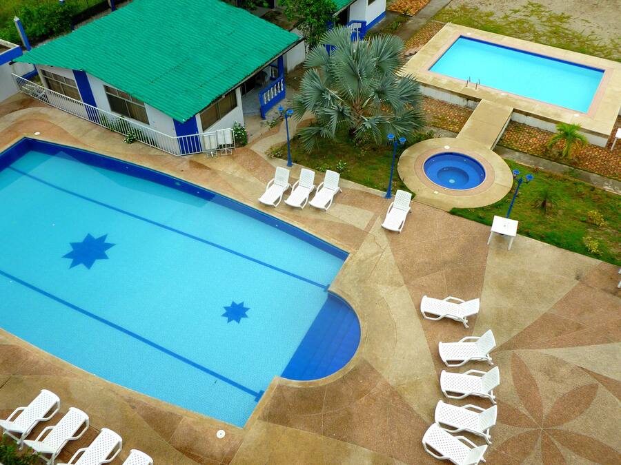 A large swimming pool with lounge chairs and a smaller pool, surrounded by a landscaped area with palm trees.