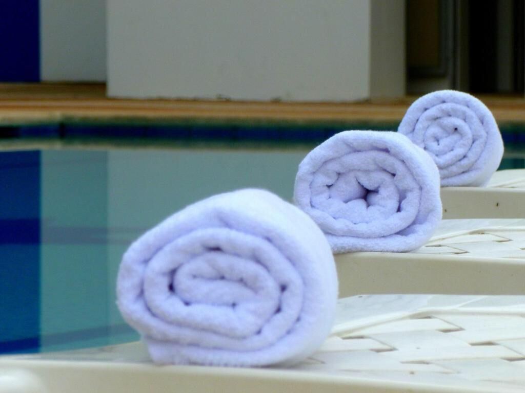 Three rolled towels placed on a white surface near a pool.