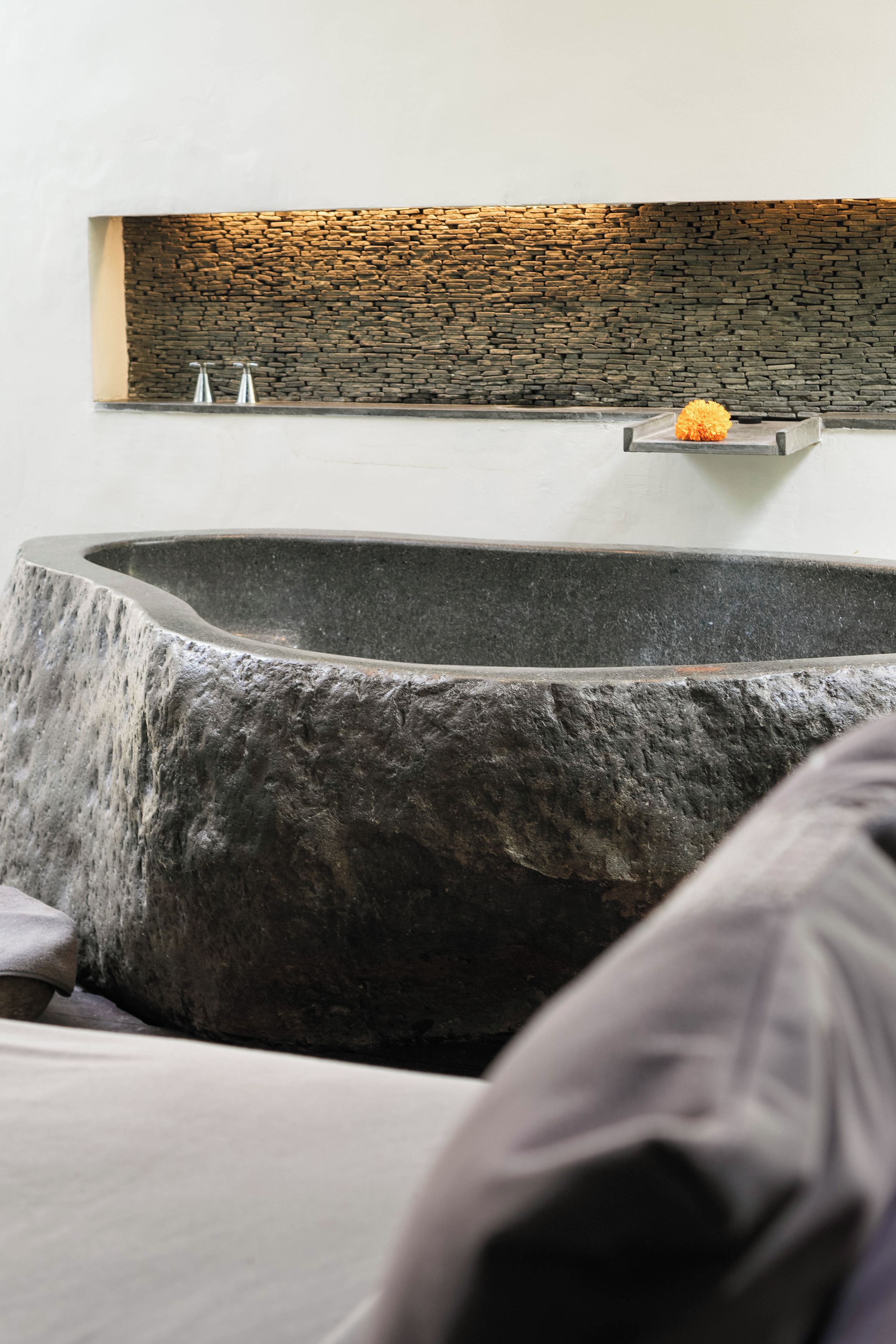 Un baño moderno con un lavabo de piedra, un estante empotrado con una flor y una pared de piedra.