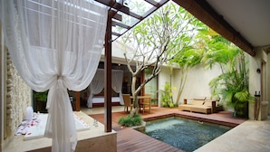 A serene outdoor pool area with a wooden deck, a small seating area, and a canopy. - The Amala Boutique Retreat (Seminyak)
