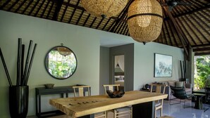 A modern dining area with a wooden table, benches, and a round mirror on the wall. - The Amala Boutique Retreat (Seminyak)